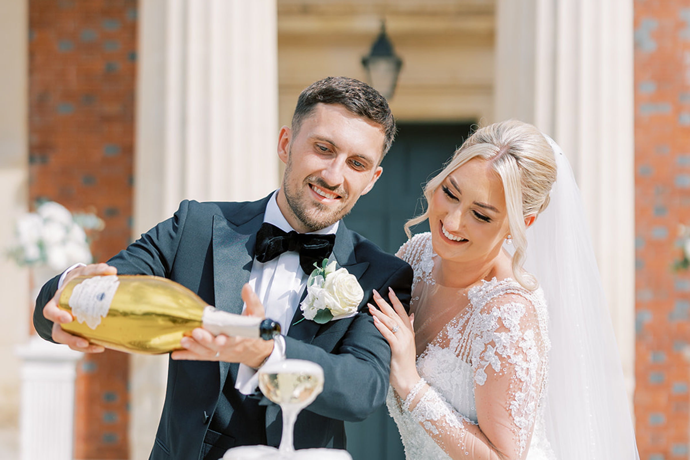 A bride and groom pouring champagne together into a glass tower at Goodnestone Park