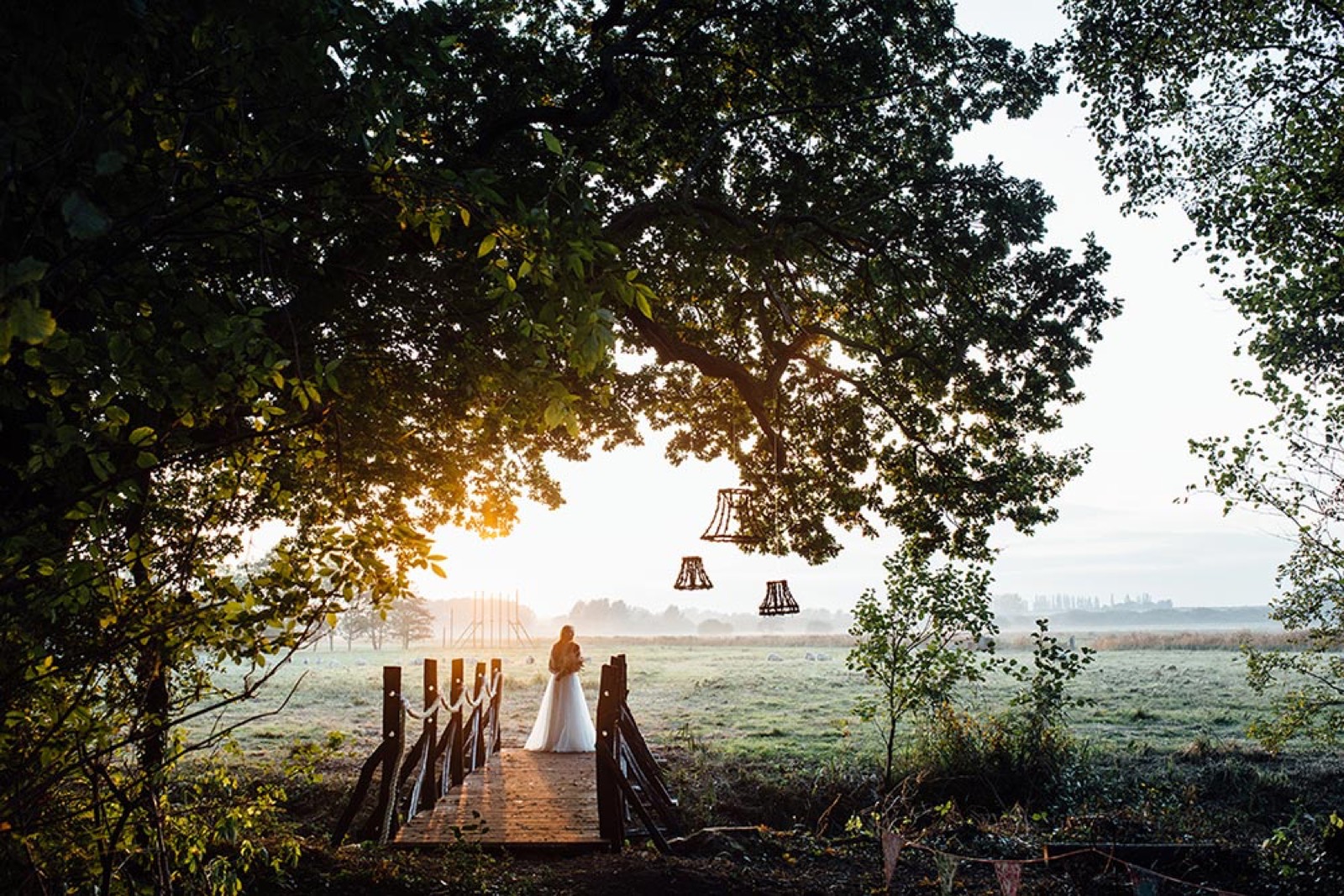 A wedding couple on a woodland bridge overlooking the Wilderness meadow at sunset