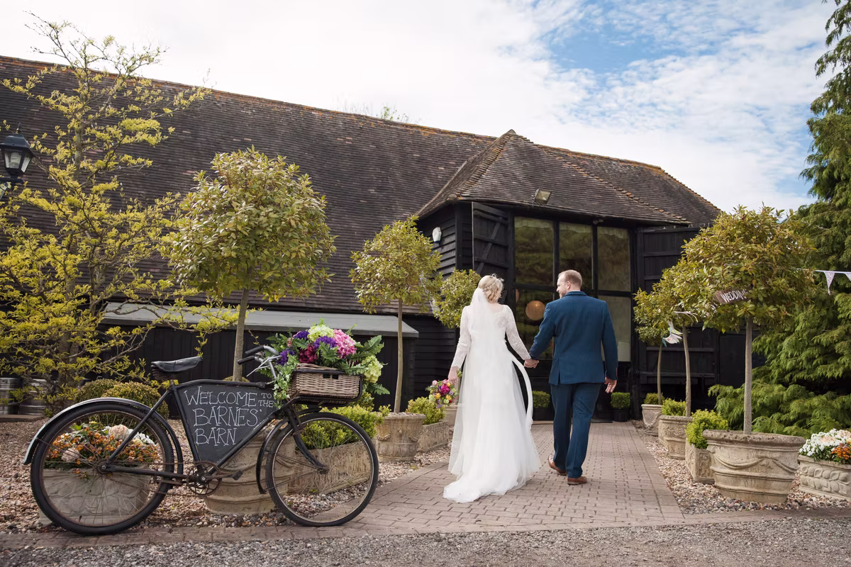 A wedding couple walking towards Winters Barns beside the flower-decorated bicycle