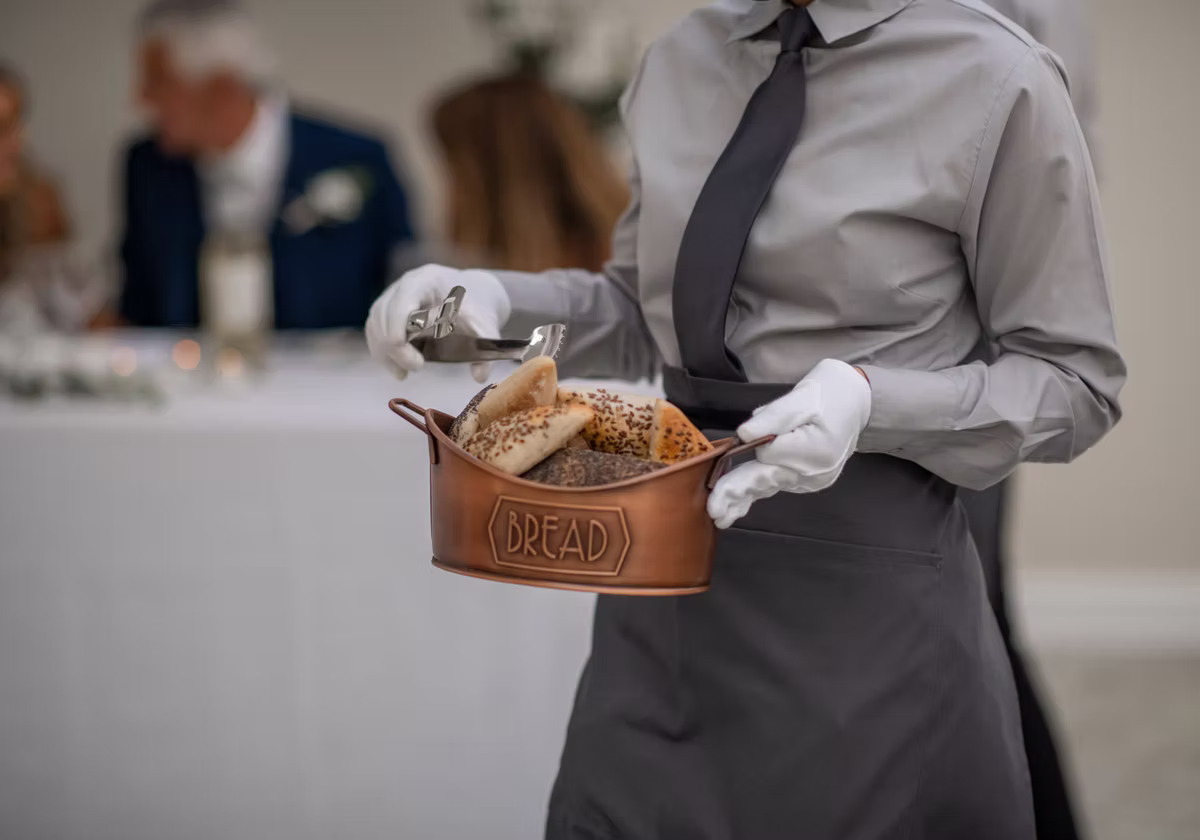 A member of the service team offering a basket of bread
