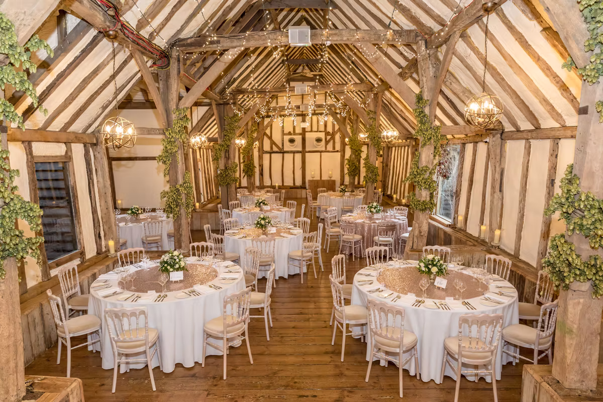 Round tables set for a wedding breakfast beneath the barn beams at Winters Barns