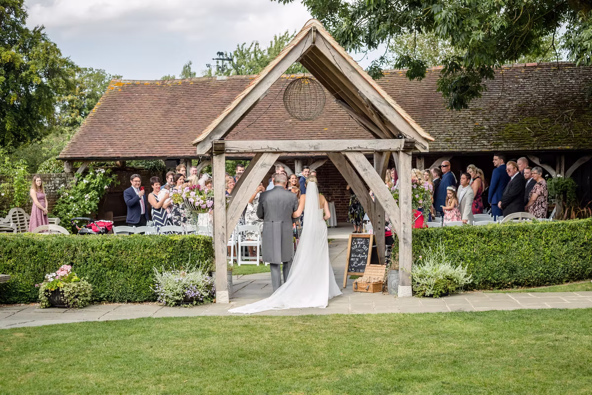 An outdoor wedding ceremony beneath the timber shelter at Winters Barns
